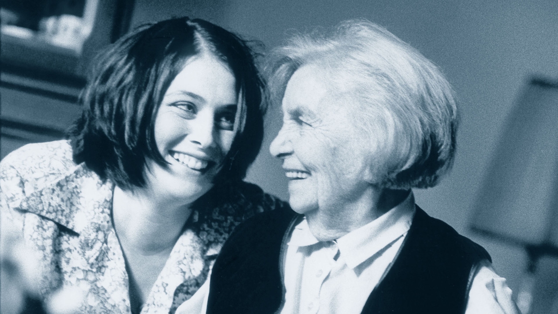 Eine ältere und eine jüngere Damen schauen sich gegenseitig mit einem Lächeln an.